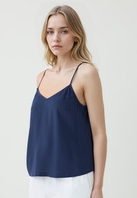 Marineblauwe, lichte camisole-top met dunne spaghettibandjes, V-hals en subtiele textuur; heeft een zak aan de linkerkant.