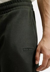 Ciemnozielone dresy z elastycznym pasem, bocznymi kieszeniami i teksturowanym materiałem. Posiadają naszytą metkę z logo na lewym udzie.