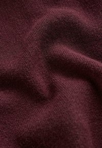 Țesătură burgundă cu o suprafață moale și texturată, având nervuri fine și un aspect ușor întins, punând în evidență materialul său confortabil.