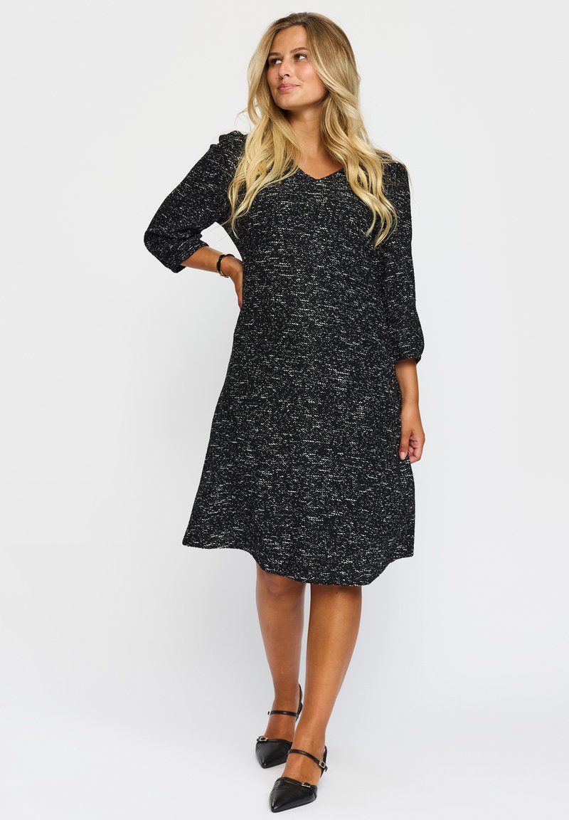 Svart och vit stickad klänning med trekvartslånga ärmar, V-halsringning och utsvängd fåll. Mönstret har en strukturerad, prickig look.