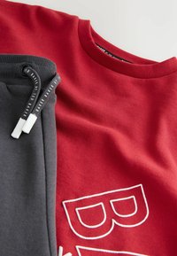 Red cotton t-shirt with white embroidered letter 'B' and gray sweatpants with black drawstring and white tips, laid flat.