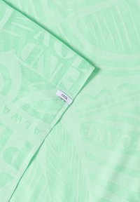 Écharpe vert menthe clair avec motifs subtils de feuilles et de texte, coin plié avec petite étiquette en tissu blanche "CECIL".