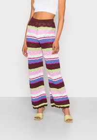 Pantalons à larges jambes au crochet, arborant de larges rayures horizontales en violet, vert, rose et marron, avec un design texturé en maille ouverte.