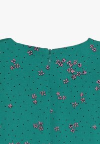 Tyrkysové šaty s malými černými puntíky a růžovými květinovými vzory. Na zadní straně je diskrétní zip na krku.