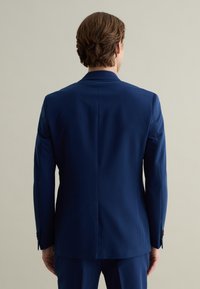 Giacca da abito blu navale con vestibilità su misura, apertura centrale sul retro e dettagli con bottoni a due. Tessuto liscio con una finitura opaca.