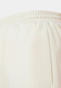 Pantalons crème à taille élastique avec poches latérales, fabriqués à partir d'un tissu doux ; texture lisse et design simple sans motifs ni accents visibles.