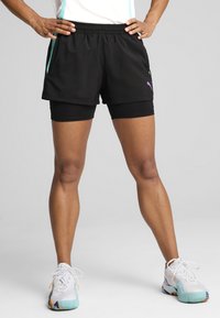 Mustad mustad lühikesed püksid, millel on lõtv lõige, teal värvi detailiga, ja need on kihitatud mustade sobivate jalgrattapükste peale. Kingad on valged, millel on värvilised detailid.