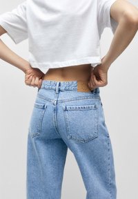 Lichtblauwe denim jeans met een hoge taille, voorzien van achterzakken en een tan leren label op de taille. De stof heeft een licht gestructureerde afwerking.