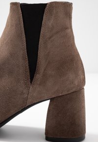 Bottines en suède marron avec un talon épais, des panneaux latéraux élastiques et une texture lisse avec des coutures visibles le long des bords.