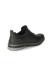 Chaussure en cuir noir avec un bout arrondi, profil bas et semelle en caoutchouc grise. Elle est dotée de lacets, d'une texture lisse et d'un design minimaliste.