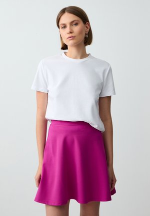 T-shirt bianco in cotone a maniche corte, abbinato a una gonna rosa svasata e lunga fino al ginocchio, realizzata in un tessuto liscio e elastico. Senza motivi.
