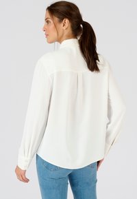 Weiße Bluse mit langen Ärmeln aus leichtem Stoff in lockerer Passform, mit Rückenausschnitt und Manschetten. Kombiniert mit hellblauen Jeans.