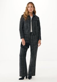 Completo in tweed bianco e nero composto da una giacca corta e pantaloni a gamba larga. Abbinato a una cintura nera e stivaletti con tacco.