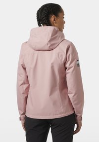 Lichtroze waterdichte jas met een capuchon, voorzien van een verstelbare manchette, een logo-opdruk op de mouw en een gladde, matte textuur.