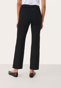 Zwarte broek met een recht broekontwerp, gladde textuur en een brede tailleband. Bevat twee achterzakken en platte, zwarte schoenen.
