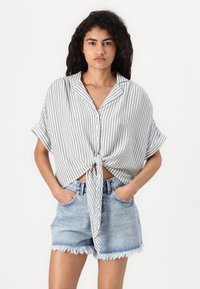 Randig kortärmad skjorta i ljusgrått och vitt, knuten vid midjan. Kombinerad med denimshorts med fransad nederkant och fickor.