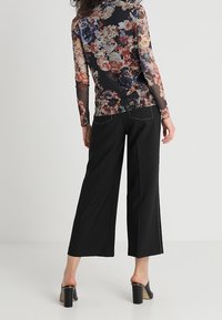 Mustat leveälahkeiset housut, jotka on yhdistetty läpikuultavaan kukkakuosisessa pitkähihassa puseroon, jossa on värikkäitä kukkia. Liukas rakenne, jossa on hienovaraisia ompelutietoja.