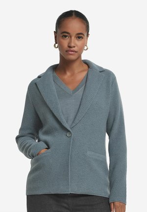 Cardigan tissé bleu clair avec col châle, fermeture à un bouton et deux poches avant. Texture douce et coupe décontractée.