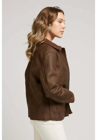 Blouson en cuir marron avec un col en shearling marron, présentant une coupe décontractée, des poches latérales et des détails de couture visibles.