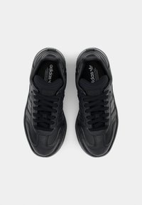 Un par de zapatillas de cuero negras de Adidas con cordones, vistas desde arriba sobre un fondo blanco liso.