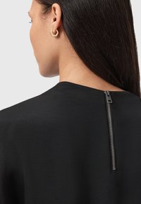 Top nero con una consistenza liscia, dotato di una zip corta sul retro. Design semplice con scollatura ampia e senza motivi visibili.