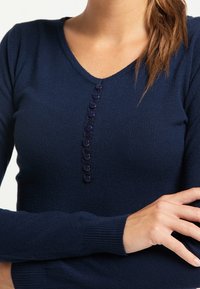 Mörkblå, figurnära tröja i mjukt material, med V-ringning, långa ärmar och en knapplist med åtta matchande knappar.