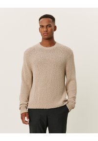 Suéter beige de punto con un patrón texturizado y elevado, y cuello redondo. Presenta mangas largas y puños acanalados.