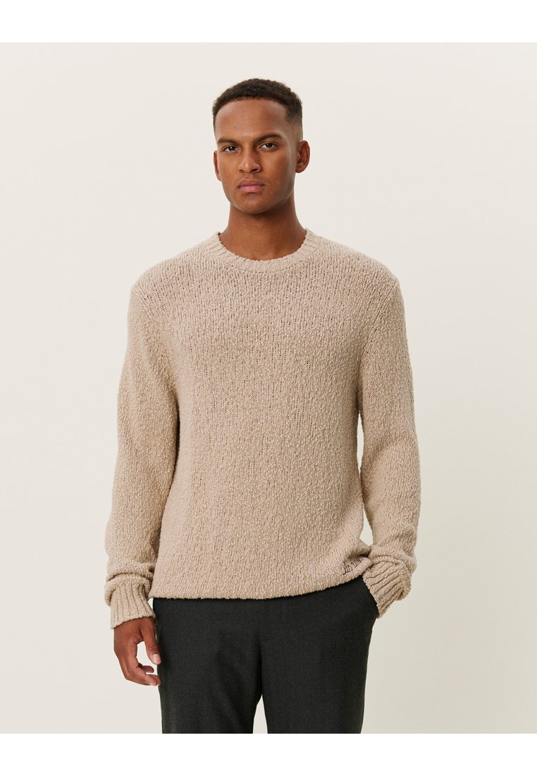 Suéter beige de punto con un patrón texturizado y elevado, y cuello redondo. Presenta mangas largas y puños acanalados.