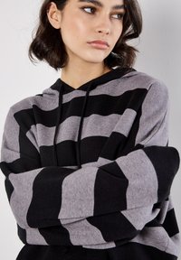 Czarny i szary pasiasty sweatshirt z kapturem o luźnym kroju, z długimi rękawami i regulowanym kapturem, wykonany z miękkiego dzianinowego materiału.