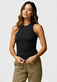 Schwarzes, geripptes Tank-Top mit hohem Hals und ärmellosem Design, kombiniert mit beigen Hosen mit einem schwarzen gepunkteten Muster.