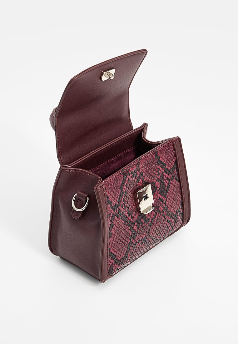 Sac à main bourgogne avec motif serpent, surface texturée, fermeture à clip métallisé et un anneau unique sur le côté pour l'attache de la bandoulière.