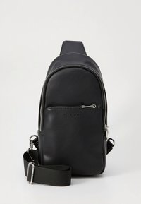 Zwarte leren rugzak met een afgerond ontwerp, een voorvak met ritssluiting en een verstelbare stoffen riem. Voorzien van hardware in zilverkleur en een logo.