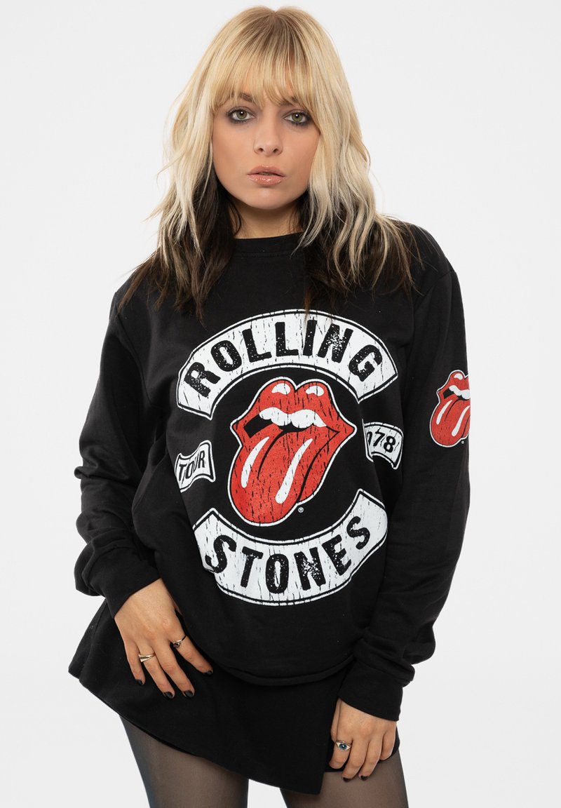 Black long-sleeve sweatshirt featuring Rolling Stones logo in red and white, with vintage textured graphics and a small logo patch on the right sleeve.