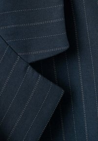 Tissu bleu marine foncé avec fines rayures blanches, montrant des bords pliés et des détails de couture sur une surface textile texturée.