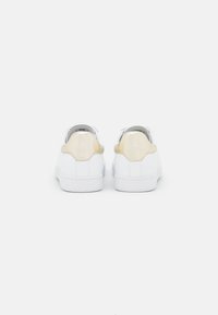 Białe trampki z gładkiej skóry, z beżowym akcentem na pięcie oraz wytłoczonym logo. Płaska, biała gumowa podeszwa.