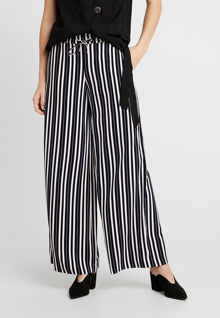 Svarta och vita randiga vida byxor med dragsko i midjan och slät tyg, tillsammans med svarta spetsiga klackskor.