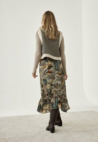 Jersey de punto con un diseño texturizado en gris y crema; falda maxi con estampado floral en tonos tierra; botas de cuero marrón hasta la rodilla.