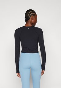 Juoda ilga rankovė viršūnė su prigludusia išvaizda, lygiu paviršiumi ir maža emblema gale, derinama su šviesiai mėlynomis prigludusiomis leggins.
