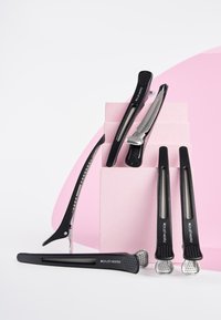 Set med svarta hårklämmor och verktyg på en rosa block. Innehåller metalliska detaljer, texturerade grepp och slanka, förlängda former.