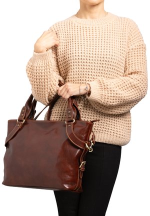 Borsa a tracolla in pelle marrone con manici doppi, con accenti in ottone e cuciture. Maglione beige intrecciato indossato da una persona che tiene la borsa.
