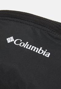 Țesătură neagră cu o textură netedă, având un logo alb "Columbia" și un sistem de închidere cu fermoar pe marginea de sus.