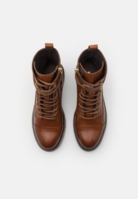 Bottines en cuir marron avec fermeture à lacets à l'avant, bout renforcé, accessoires dorés et doublure intérieure texturée.