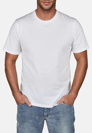 Weißes Baumwoll-T-Shirt mit Rundhalsausschnitt und kurzen Ärmeln, präsentiert an einem Modell, das Jeans trägt und die Hände in den Taschen hat.