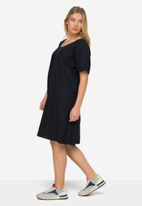 Černé šaty s krátkým rukávem, se splývavým výstřihem do V, dlouhé po kolena a s pohodlným střihem. Doplněné o světle modré a žluté tenisky s vícebarevnými akcenty.