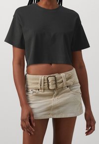 Svart kort t-shirt i bomull med korta ärmar, kombinerad med en beige manchester minikjol som har ett brett bälte och framfickor.