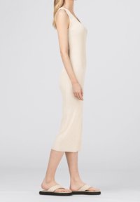 Ribbade, ärmlösa midiklänning i ljusbeige, med en figurnära silhuett och rundad halsringning. Kombinerad med flata, ljusa sandaler.