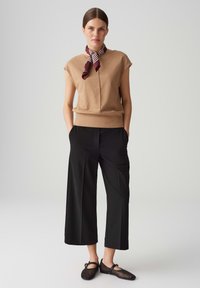 Beige gebreide top met korte mouwen, gecombineerd met zwarte wijde broek. Accessoires zijn een bordeauxrode en witte gestreepte sjaal om de nek. Zwarte mesh flats.