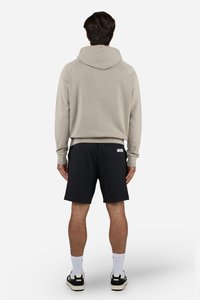 Felpa con cappuccio beige chiaro, dal taglio relax, abbinata a pantaloni corti neri. Caratteristiche includono polsini a costine e un'etichetta logo sui pantaloni.