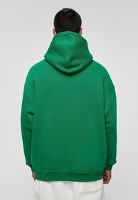 Groene sweatshirt met een capuchon, met een ontspannen pasvorm, geribde manchetten en een soepele, textuurstof. De achterkant toont minimale ontwerpelementen.