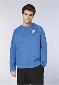Blauer Pullover aus Baumwolle mit Rundhalsausschnitt und gerippten Bündchen. Ein kleines Patch-Logo befindet sich auf der linken Brust.